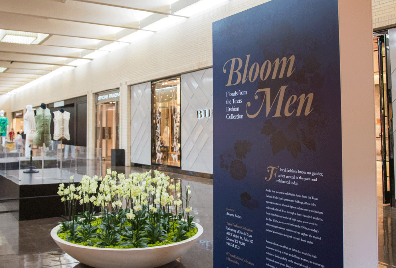 Exhibition plinth with text next to planter and platforms with men's garments