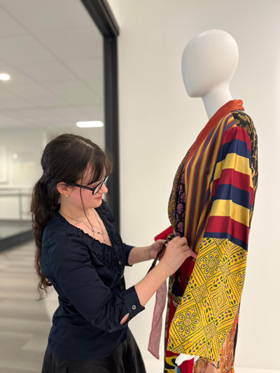 Woman ties a sash of a robe on a mannequin.