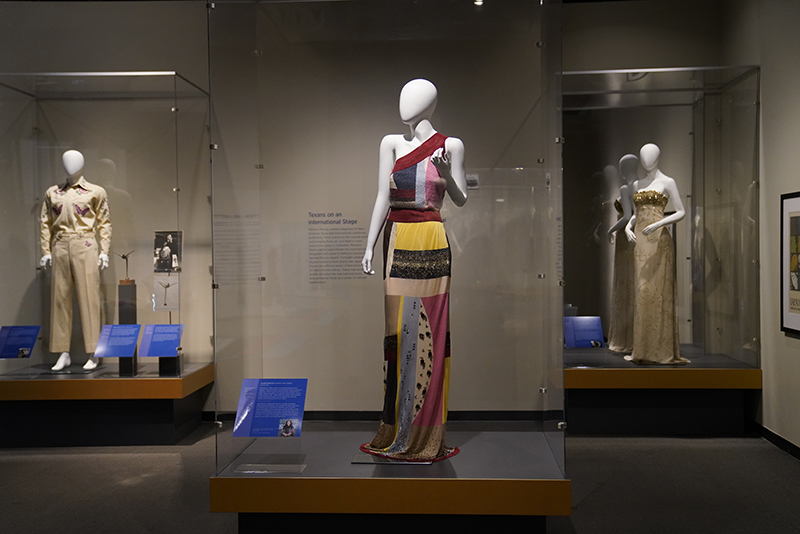 Gallery with three cases featuring a western-style suit and two evening dresses